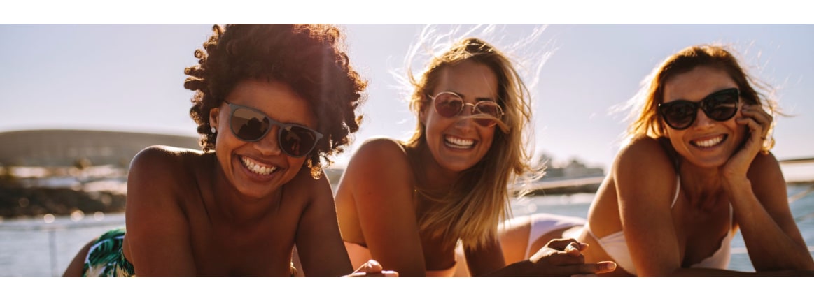 drei frauen liegen im bikini auf einem steg am wasser in der sommer sonne