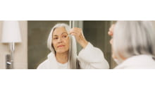 ältere frau mit langen grauen haaren tropft mit einer pipette serum auf ihr gesicht