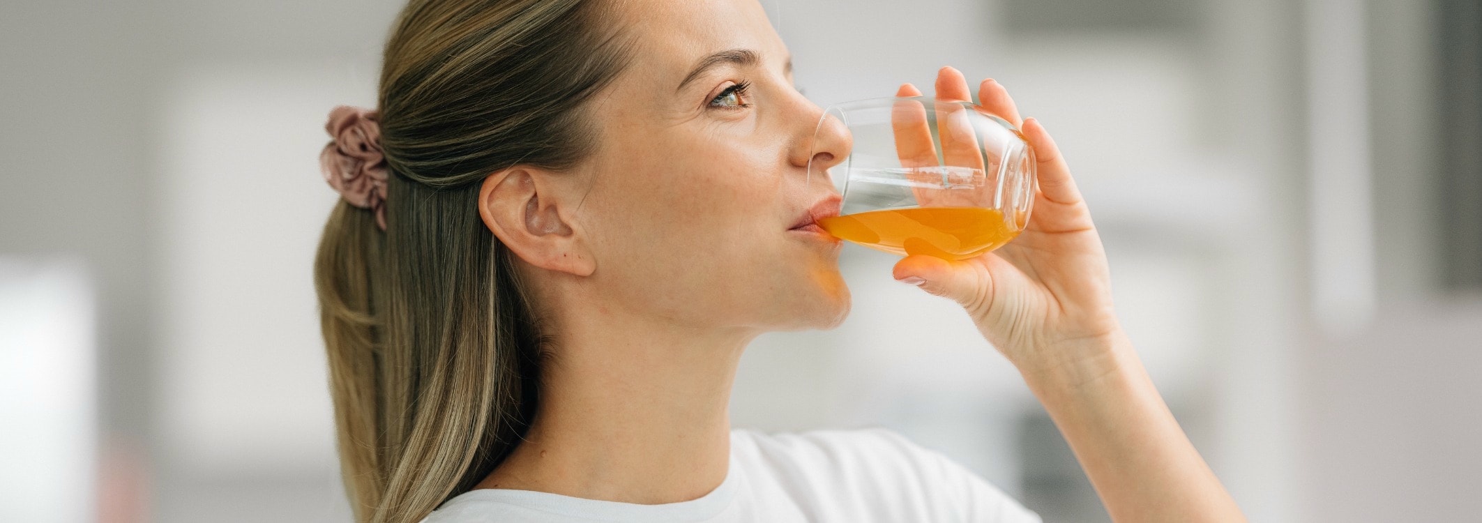 junge blonde frau trinkt orangefarbene flüssigkeit aus einem glas